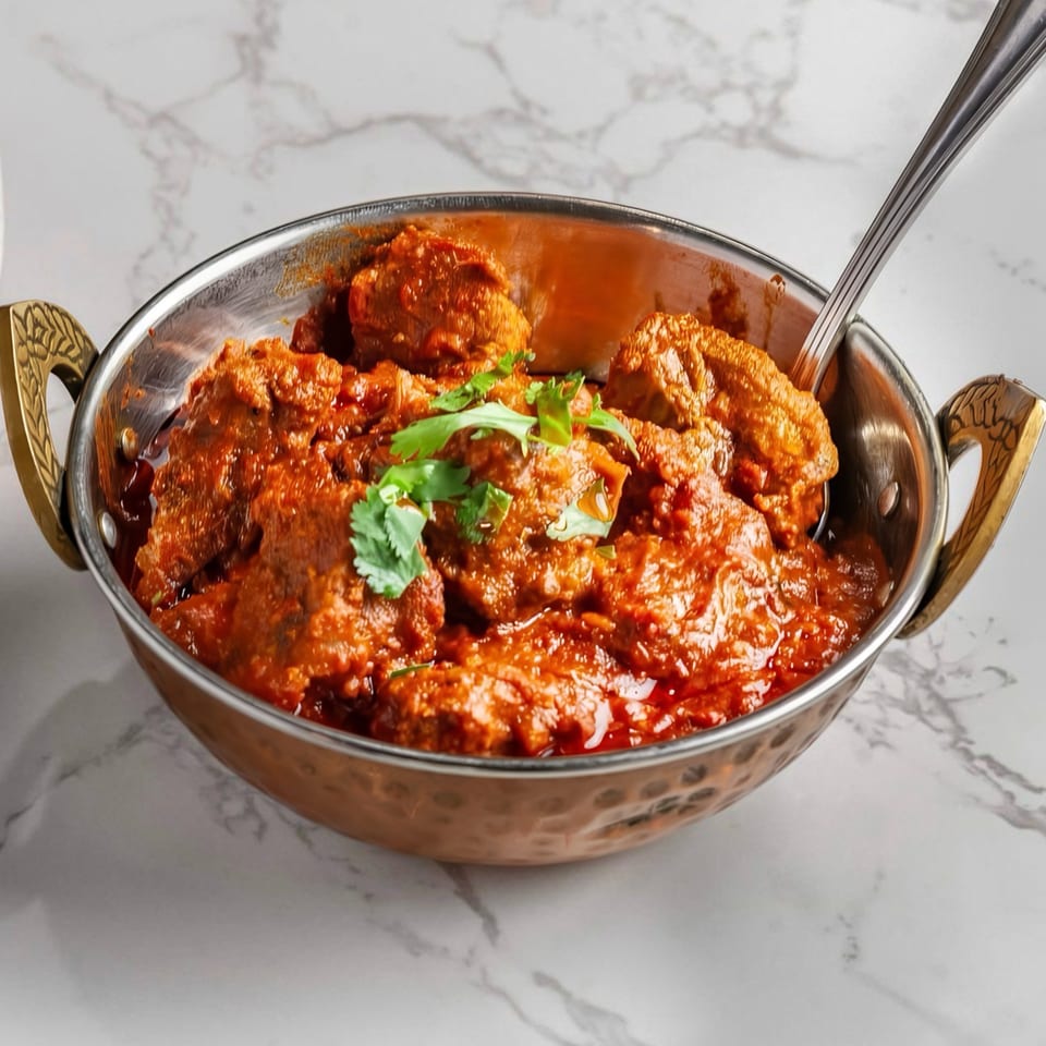 A copper bowl filled with a rich red curry, garnished with fresh cilantro, on a marble surface.