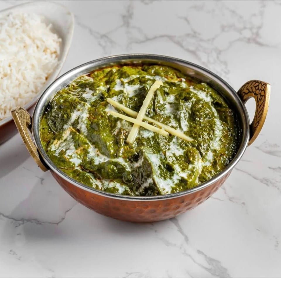 Palak Paneer in a copper bowl with white rice on a marble surface.